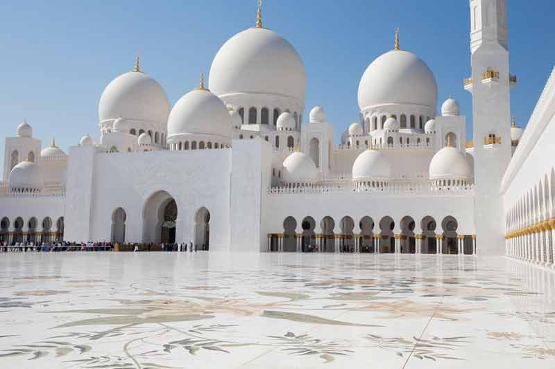 Vue extérieure de la grande mosquée Sheikh Zayed à Abu Dhabi avec ses dômes blancs et sa cour ornée de motifs floraux