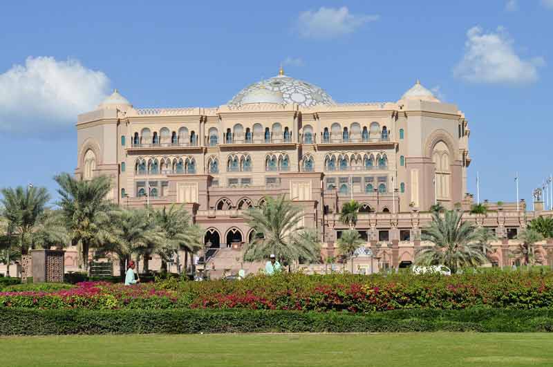 Façade de l'Emirates Palace à Abu Dhabi, entourée de jardins fleuris et de palmiers sous un ciel bleu