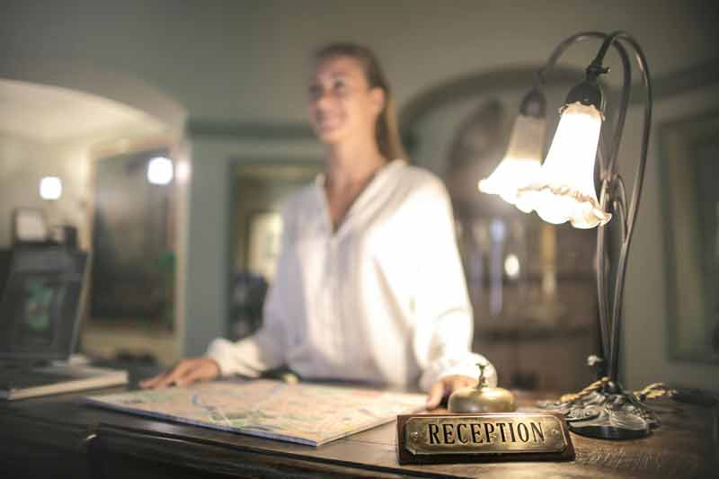 Réceptionniste accueillant les voyageurs dans un hôtel, avec une carte sur le comptoir et une ambiance chaleureuse