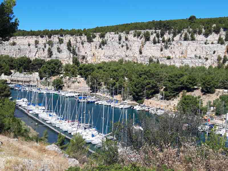 Vue sur le port de plaisance de la calanque de Port-Miou à Cassis, entouré de falaises calcaires et de pins méditerranéens