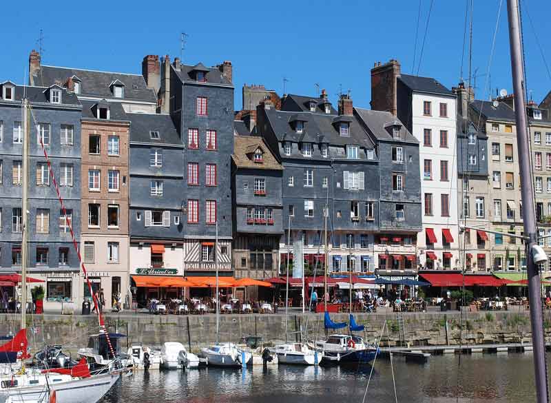 Alignement de maisons à colombages et en ardoise typiques de Honfleur, bordant le Vieux Bassin animé de terrasses de cafés