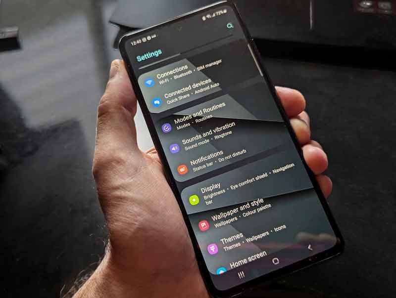 main tenant un smartphone affichant le menu des paramètres Android, avec les options de connexion et d’affichage