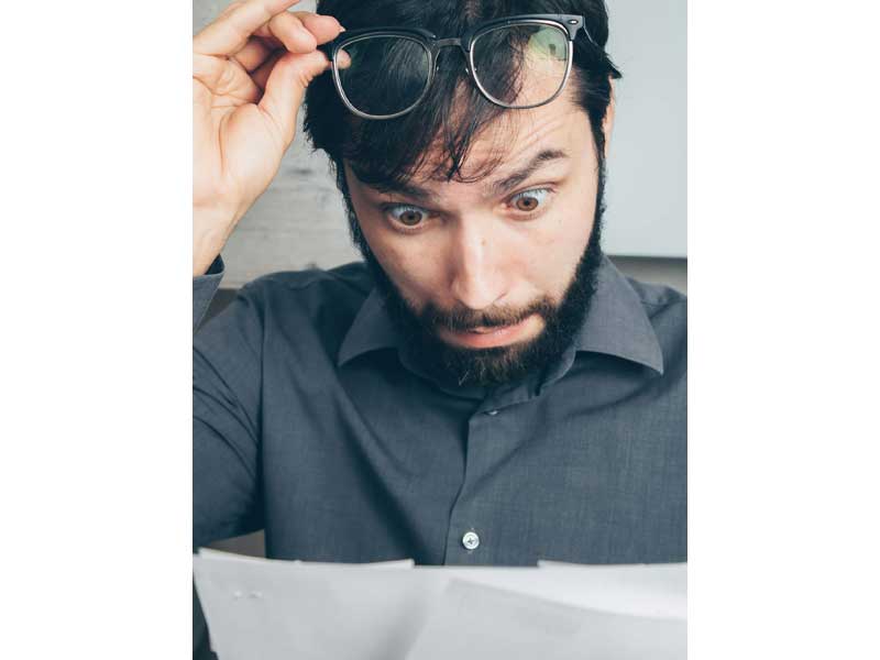 homme levant ses lunettes avec un air surpris en regardant une facture de téléphone
