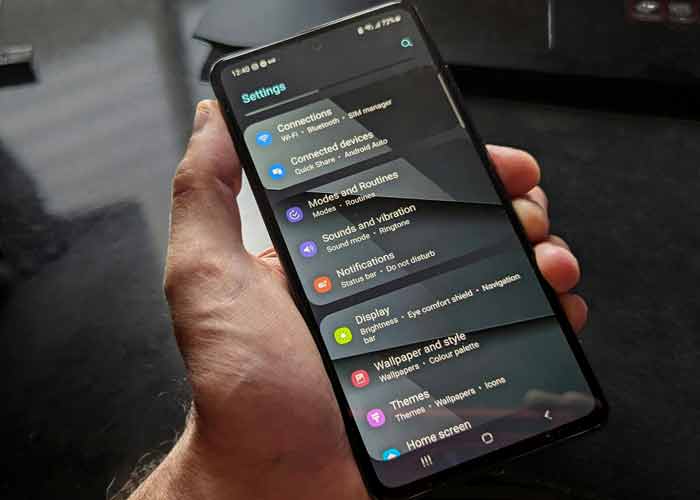 Main tenant un smartphone affichant le menu des paramtres Android, avec les options de connexion et daffichage