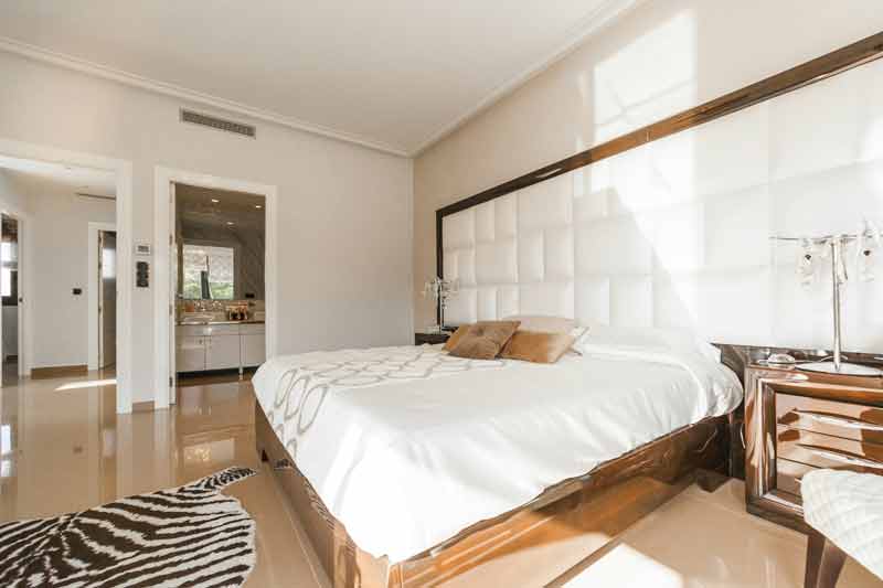 Chambre luxueuse réservée avec une carte cadeau. Elle dispose d'un grand lit, d'une tête de lit matelassée blanche, de 
							coussins dorés et une lumière naturelle entre par la fenêtre. Une salle de bain est visible en arrière-plan