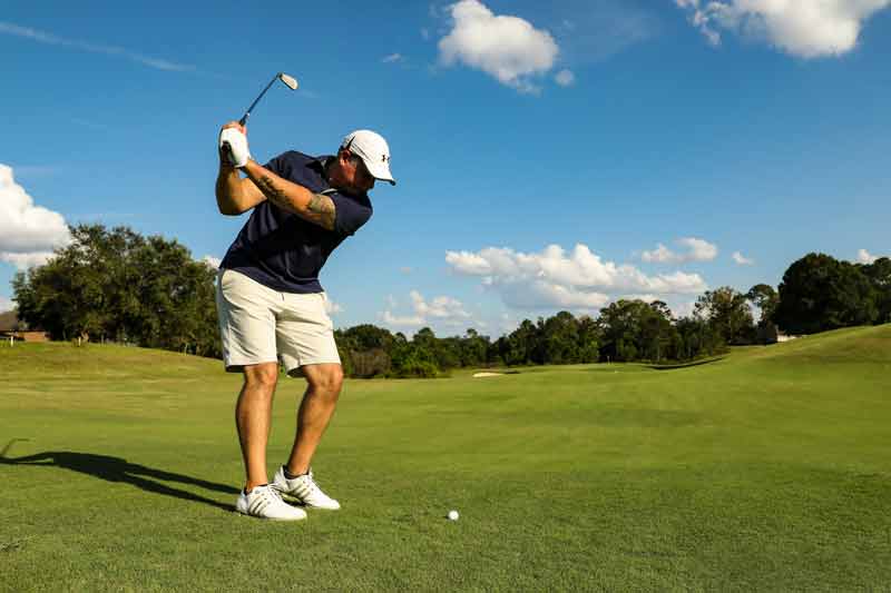 Golfeur en pleine action sur un parcours verdoyant prêt à frapper la balle