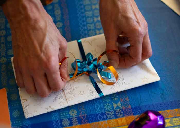 Gros plan sur des mains attachant un ruban bleu et orange autour d'une carte cadeau soigneusement 
						emballe dans du papier blanc dcor d'toiles dores, pos sur une nappe bleue festive