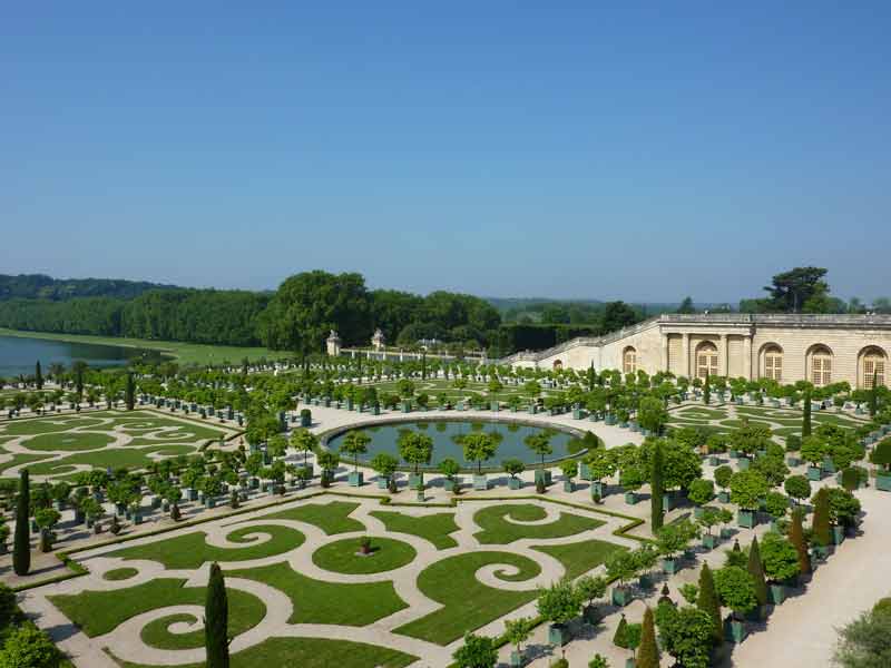 Les jardins à la française du château de Versailles avec ses parterres géométriques, bassin rond et orangerie sous un ciel bleu clair