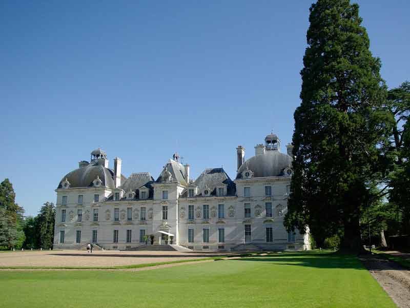 Façade élégante du château de Cheverny sous un ciel bleu, entourée de pelouses impeccables et d’arbres centenaires