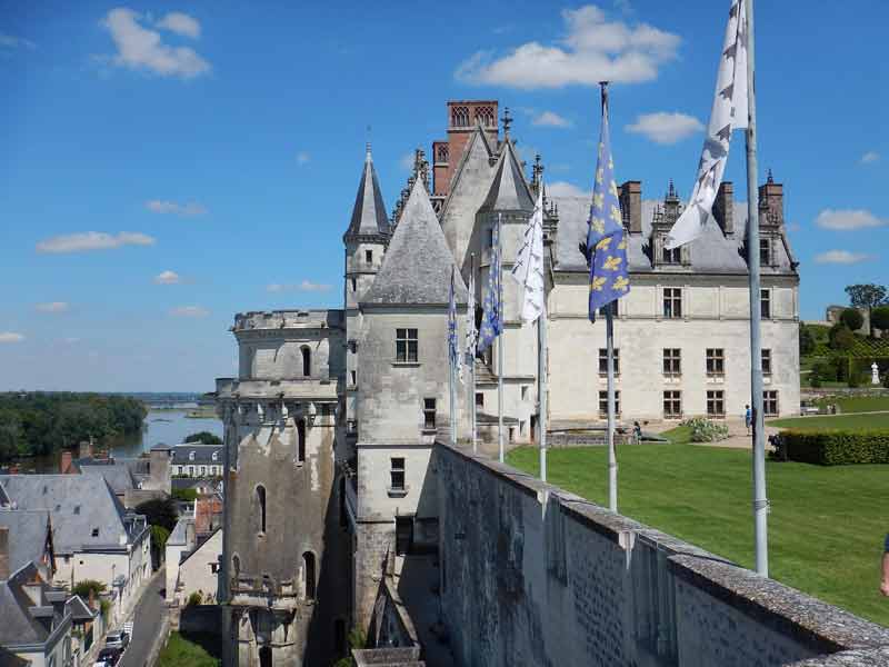 Vue latérale du château royal d'Amboise dominant la Loire, avec ses drapeaux flottants et son jardin en terrasse sous un ciel bleu
