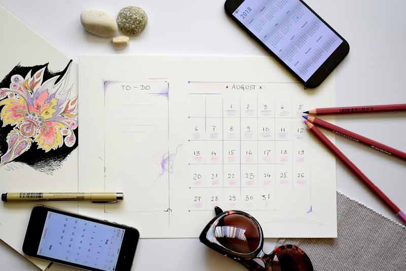Planification de vacances avec calendrier, smartphone, lunettes de soleil et crayons disposés sur une table
