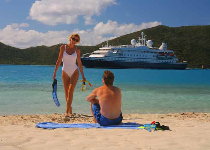 Photo d'une jeune femme en maillot de bain une pice qui sort de la mer avec des palmes  la main, avec un bateau de croisire pour clibataires en arrire plan
