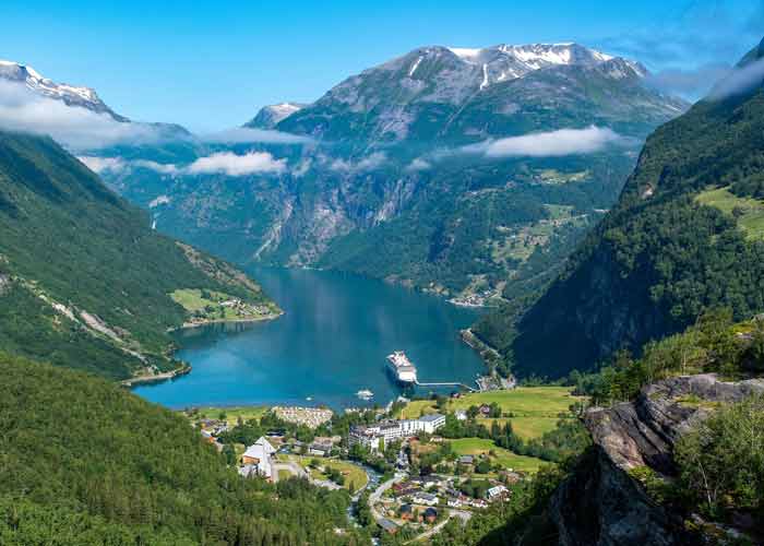 Vue panoramique sur le fjord de Geiranger en Norvge avec un navire de croisire amarr, entour de montagnes verdoyantes et de sommets enneigs lors d'une mini-croisire