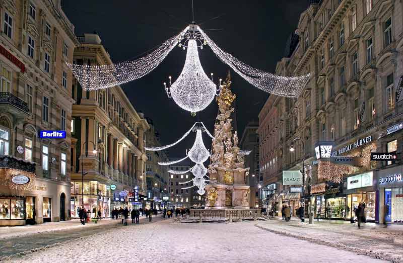 Lustres lumineux de Noël suspendus au-dessus du Graben enneigé à Vienne, avec la colonne de la Peste au centre, pour un city break en décembre