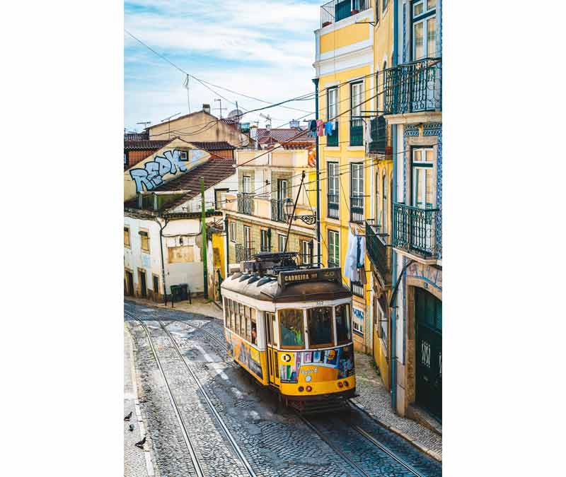 Tramway jaune dans une rue pavée en pente de Lisbonne, entre façades colorées et balcons en fer forgé, pour un city break doux en décembre
