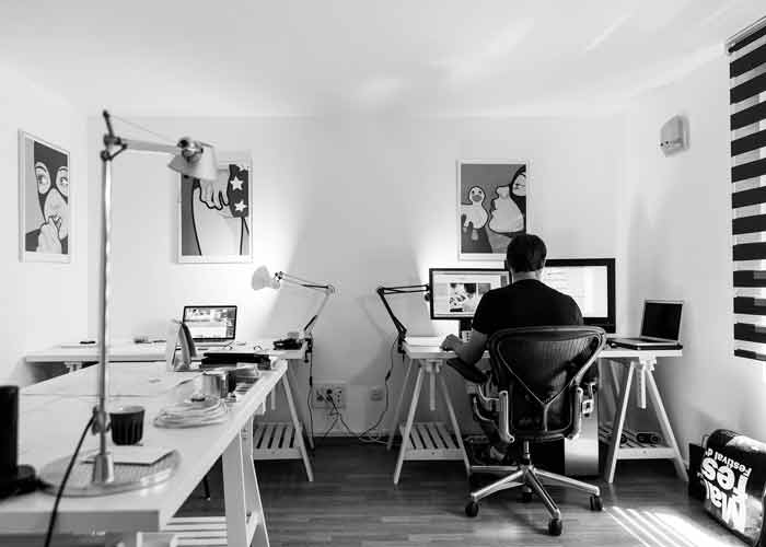 Homme qui retouche des photos sur son ordinateur dans un bureau moderne en noir et blanc, entouré d'affiches pop