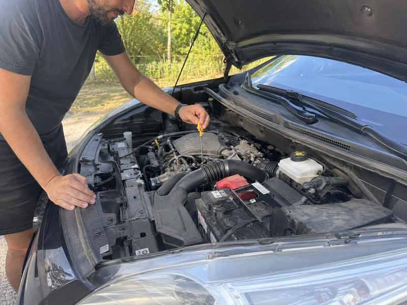 Homme vérifiant le niveau d'huile moteur de sa voiture avant un road trip
