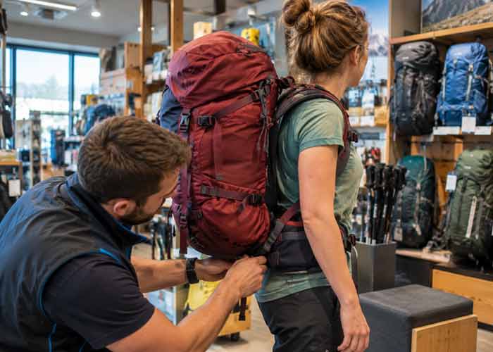 Vendeur r�glant la ceinture lombaire d'un sac � dos de voyage rouge sur une cliente en magasin pour ajuster le portage