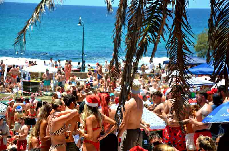 Foule de jeunes en maillot de bain célébrant le spring break sur une plage ensoleillée, face à l'océan