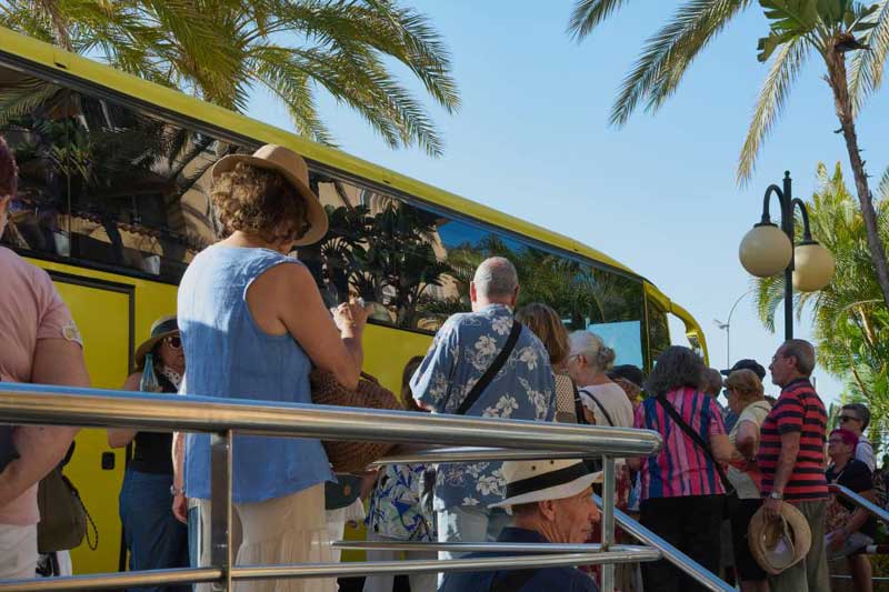 Groupe de voyageurs montant à bord d’un autocar jaune sous les palmiers pour un transfert de groupe en autocar