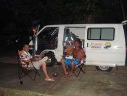 Voyageurs qui boivent un verre devant leur van aménagé la nuit