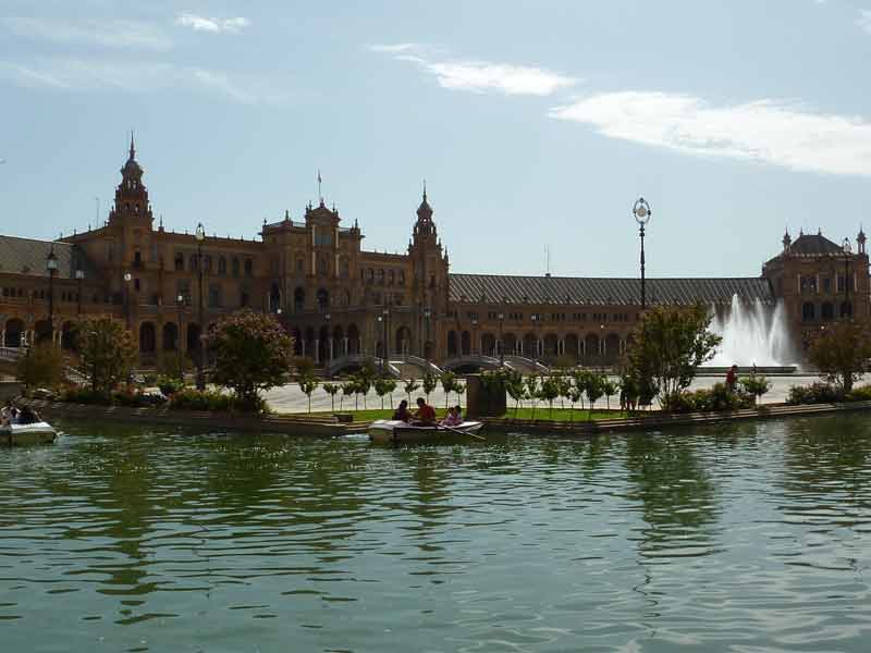 Plaza de España à Séville, avec sa fontaine centrale, ses bâtiments néo-mudéjars et sa rivière bordée de barques sous un
ciel ensoleillé.
