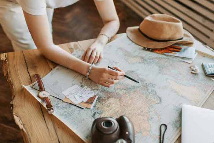 Personne planifiant un voyage sur une carte du monde avec un stylo, entoure d'accessoires comme un chapeau, une montre et un appareil photo