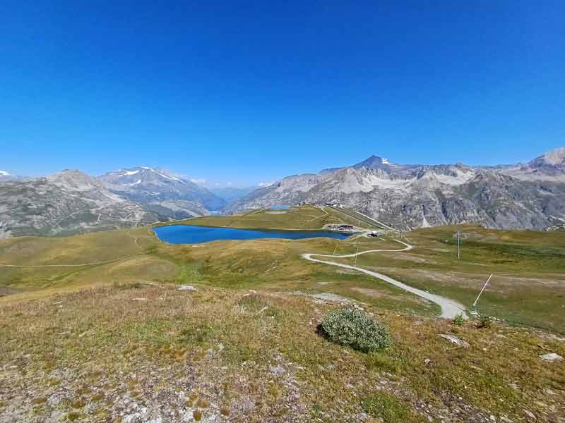 Lac d'altitude aux eaux bleu profond niché dans un alpage verdoyant, entouré de sommets enneigés sous un ciel estival 
							sans nuage, Alpes, France