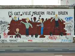 Graffiti sur l'East Side Gallery d'Ines Bayer et Raik Hönemann (Es gilt viele Mauern abzubauen) représentant des hommes et des femmes en train de détruire un mur