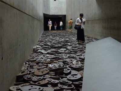 Installation Shalechet de Menashe Kadishman : dix mille visages découpés dans des disques d’acier jonchant le sol du Memory Void