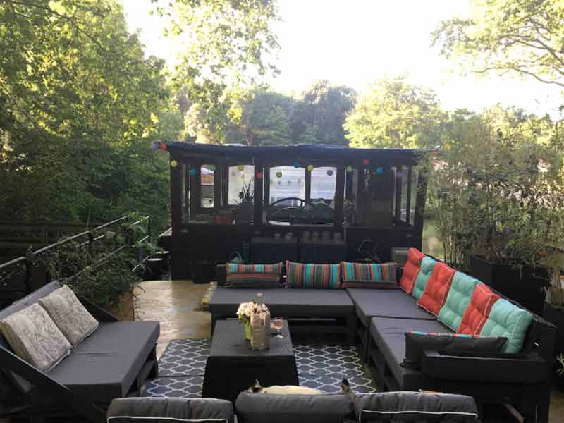 terrasse d'une péniche entourée d'arbres et d'une nature luxuriante