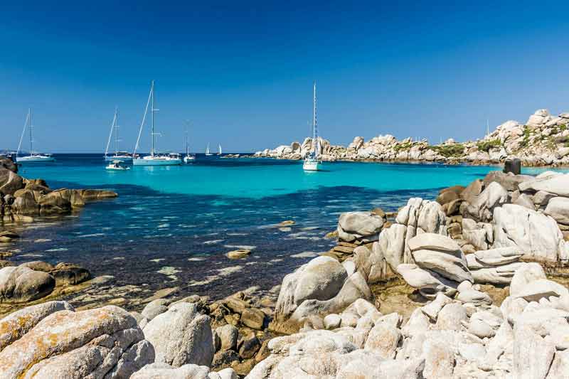 Paysage paradisiaque des îles Lavezzi en Corse, avec une eau turquoise, des rochers granitiques et des voiliers ancrés au large sous un ciel bleu