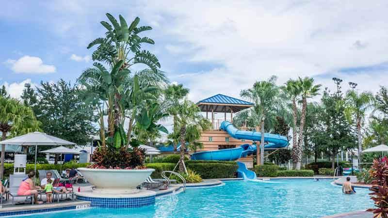 Parc aquatique de camping avec grande piscine, toboggan et palmiers dans une ambiance vacances