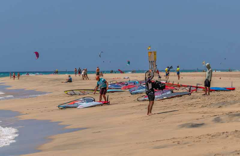 Planches de windsurf et cerfs-volants de kitesurf sur une plage de sable de l'île de Sal au Cap-Vert, avec kitesurfeurs et véliplanchistes sous un ciel bleu