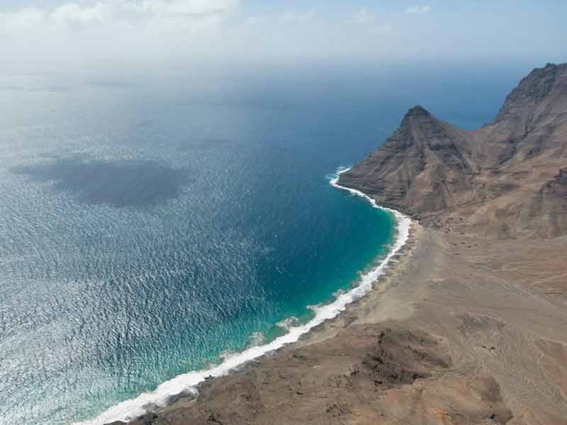 Vue aérienne d'une plage sauvage de São Vicente au Cap-Vert, encadrée par des falaises volcaniques arides plongeant dans une mer aux eaux turquoise