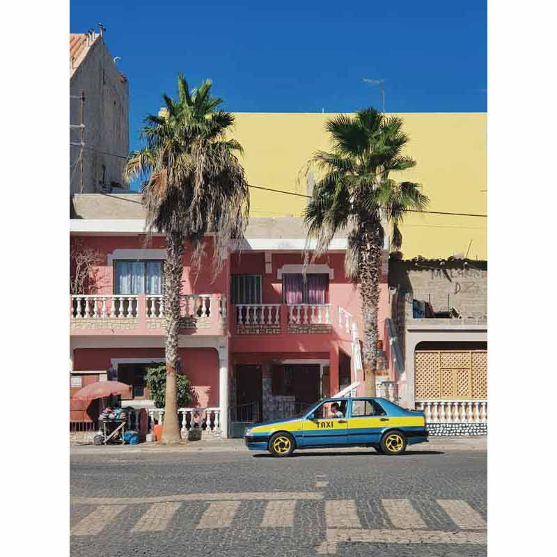 Taxi bleu et jaune garé devant une façade rose colorée de Praia à Santiago, Cap-Vert, avec palmiers et architecture coloniale portugaise