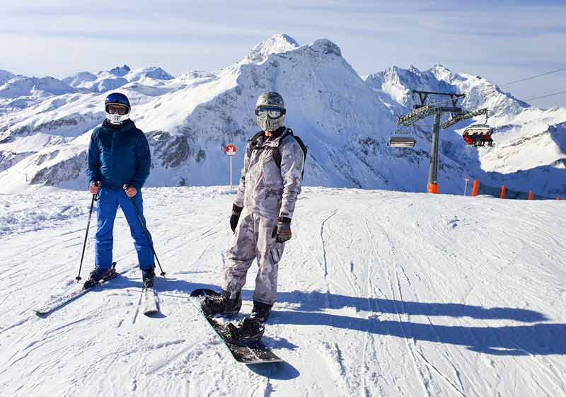 Skieur et snowboardeur au sommet d’un domaine alpin à proximité d’un chalet de luxe dans les Alpes réservé avec Le Collectionist