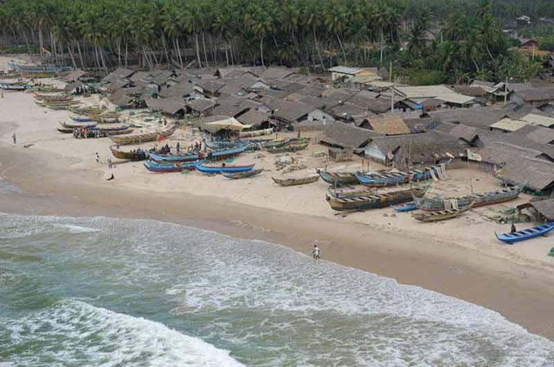 Plage d’Assinie en Côte d’Ivoire avec ses pirogues traditionnelles, ses habitations en toit de palme et ses cocotiers en arrière-plan