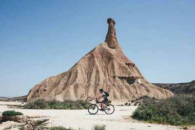 Homme faisant du vélo près d'une cheminée de fée pendant la journée dans dans la Bardena Blanca (désert de Las Bardenas Reales, Espagne