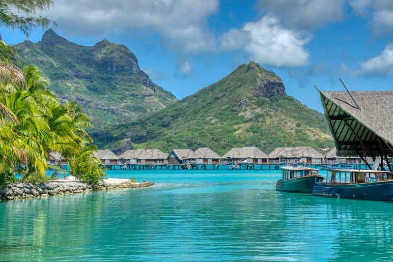 Lagon turquoise à Bora Bora avec bungalows sur pilotis et montagnes verdoyantes en arrière-plan