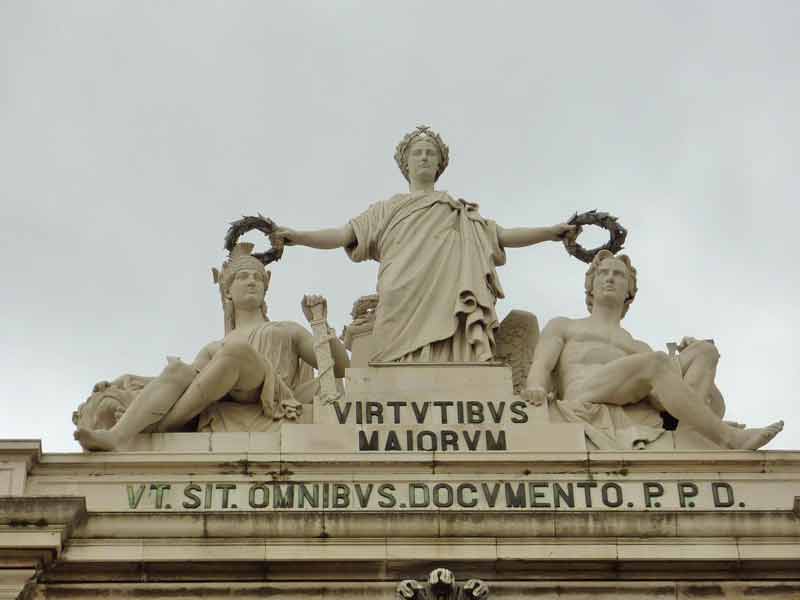 Sculptures de Célestin Anatole Calmels au sommet de l'Arc de triomphe de Lisbonne avec l'inscription du texte Les vertus des aînés, pour servir d'enseignement à tous (dédicace à la charge des dépenses publiques).