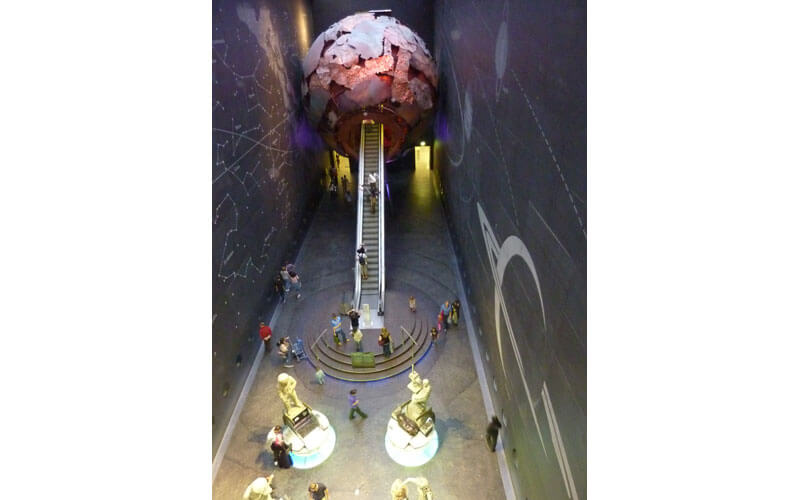 Escalator qui mène aux galeries de la zone rouge en passant par une gigantesque maquette de la Terre