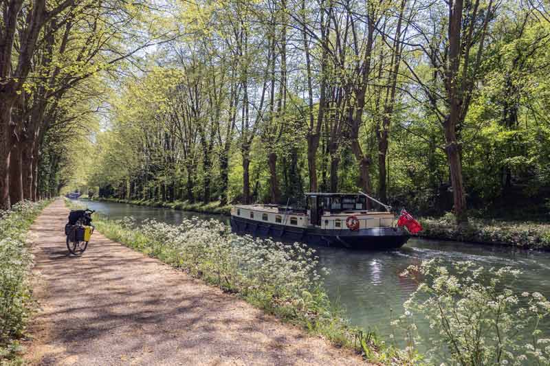Péniche et vélo sur le chemin de halage du Canal des Deux Mers dans le Lot-et-Garonne, au cœur d’un paysage printanier