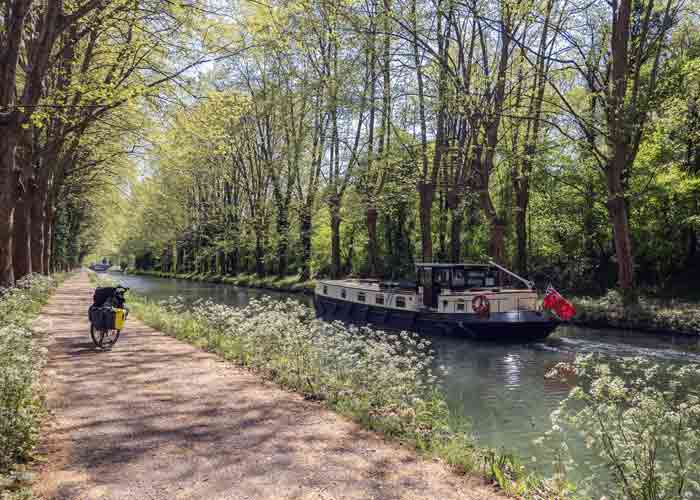 Péniche et vélo sur le chemin de halage du canal des Deux Mers dans le Lot-et-Garonne, au cœur d’un paysage printanier