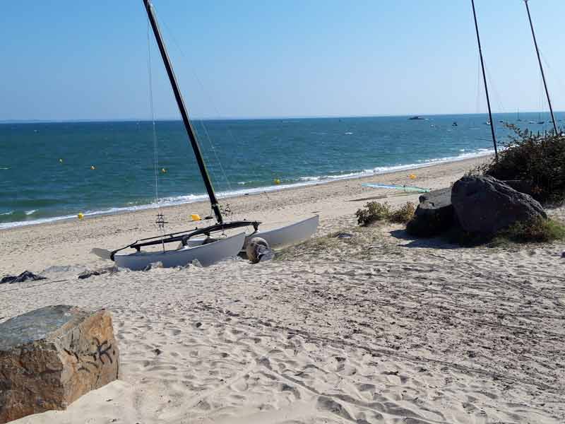 Catamaran sur le sable fin d'une plage de Noirmoutier, mer turquoise et rochers en arrière-plan