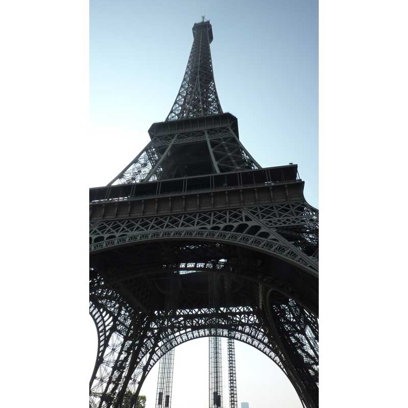 Vue en contre-plongée de la tour Eiffel depuis le sol, révélant la structure métallique emblématique du monument parisien