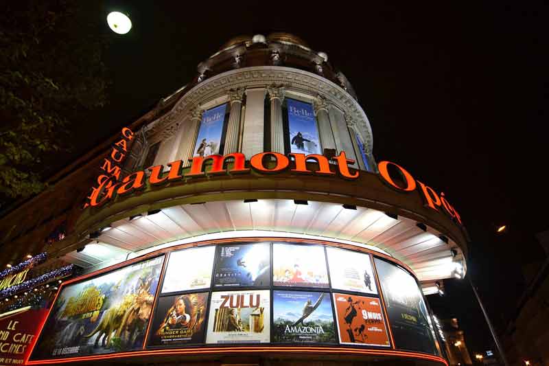 Façade illuminée du cinéma Gaumont Opéra à Paris avec affiches de films de nuit