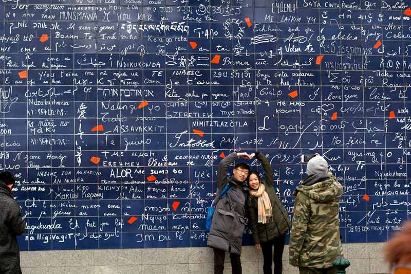 Le Mur des Je t’aime à Montmartre à Paris avec un couple amoureux posant devant les inscriptions d’amour en plusieurs langues