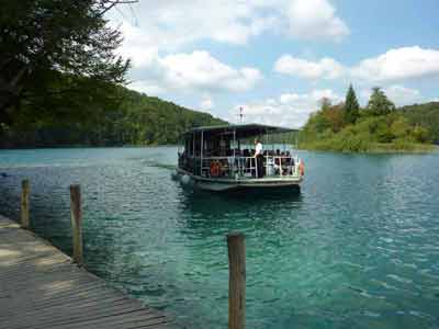 Bateau électrique transportant des visiteurs sur un lac cristallin du parc national de Plitvice, en Croatie, 
												entouré de forêts verdoyantes et d’îlots paisibles