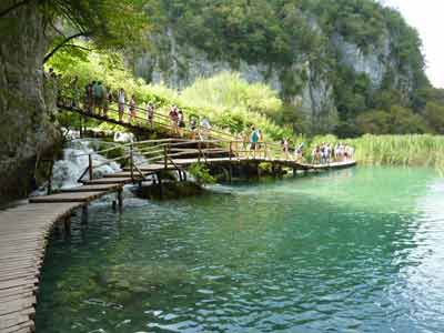 Passerelle en bois surplombant les eaux turquoise du parc national de Plitvice en Croatie, avec 
												des visiteurs en promenade lors d’un road trip en Croatie